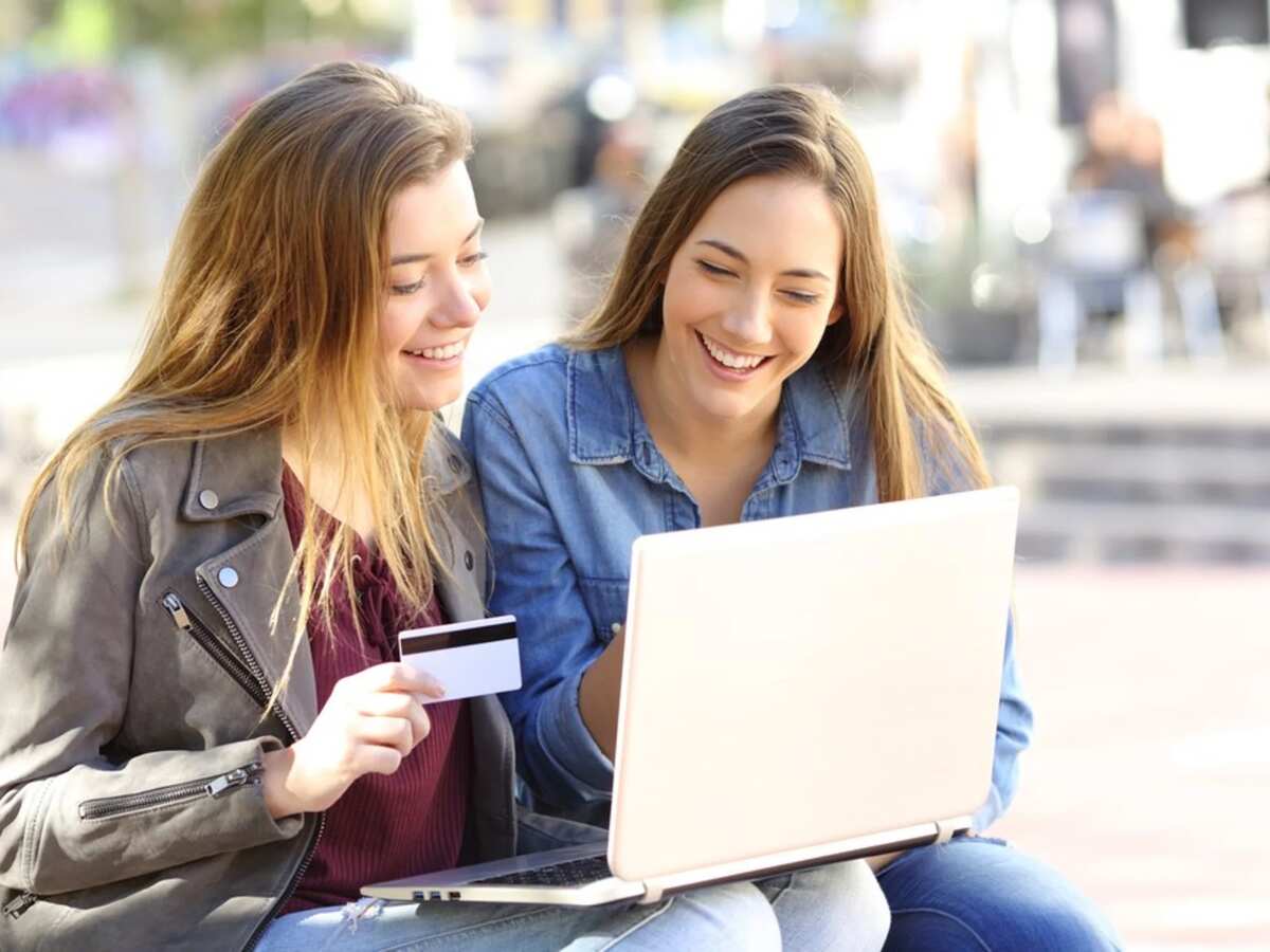 dos mujeres viendo ordenador portatil con tarjeta en la mano